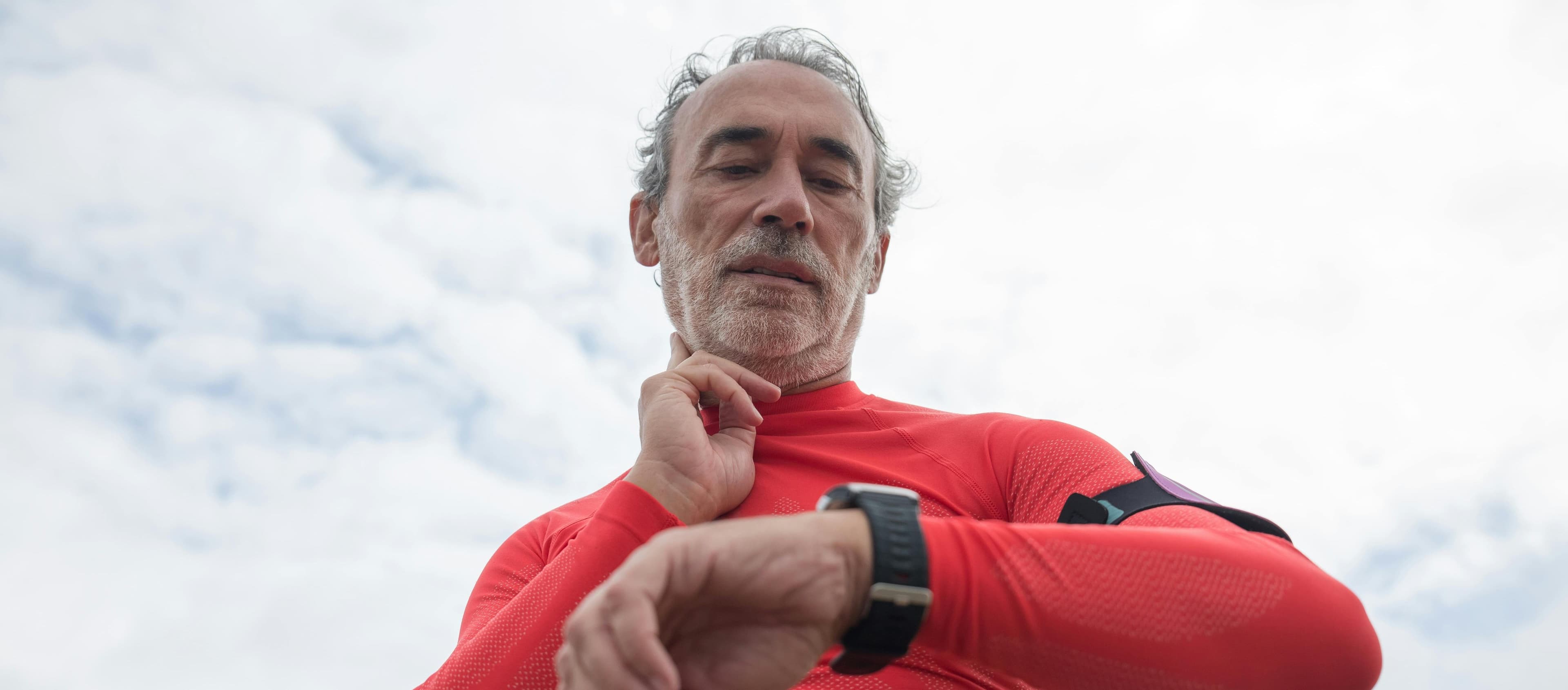 Man in red active wear checking wristwatch outdoors under cloudy sky